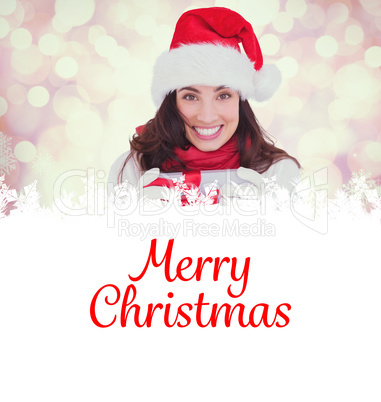 Composite image of festive brunette in santa hat holding gift