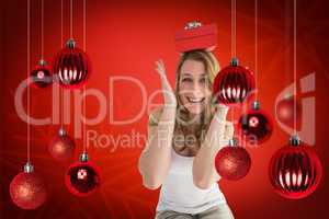 Composite image of smiling woman balancing christmas gift on her