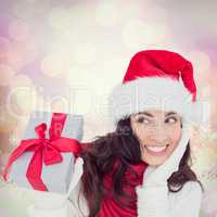 Composite image of surprised brunette in santa hat holding gift