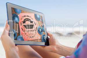 Composite image of woman sitting on beach in deck chair using ta