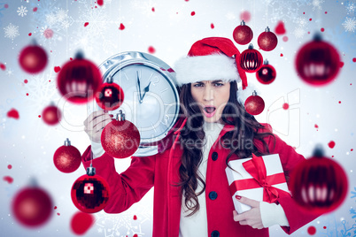 Composite image of surprised brunette holding a clock and gift