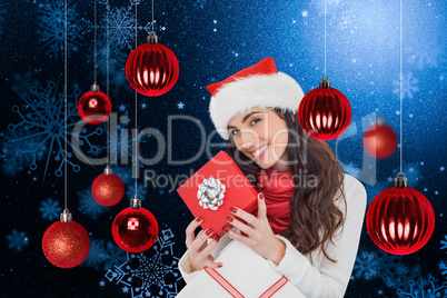 Composite image of smiling brunette holding christmas gifts
