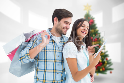 Composite image of happy couple with shopping bags and tablet