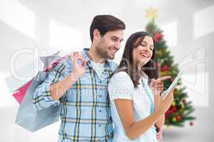 Composite image of happy couple with shopping bags and tablet