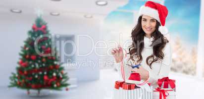 Composite image of smiling brunette in santa hat packing gifts