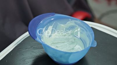 Closeup of hair dressers hand mixing solution in bowl at salon