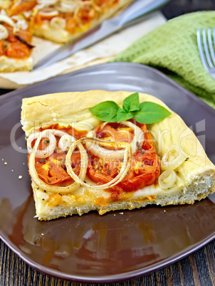 Pie with onions and tomatoes in brown plate on dark board