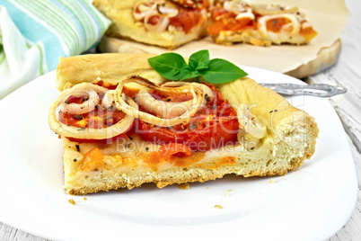 Pie with onions and tomatoes in white plate on light board