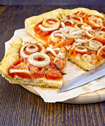 Pie with onions and tomatoes on parchment and board