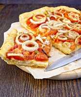 Pie with onions and tomatoes on parchment and board