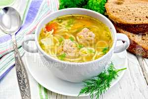 Soup with meatballs and noodles in bowl on board