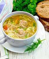 Soup with meatballs and noodles in bowl on light board