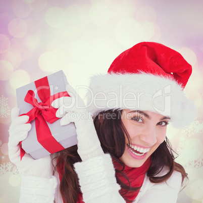 Composite image of happy brunette in santa hat holding gift