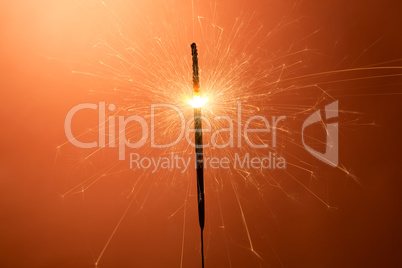 Burning sparkler on an orange background