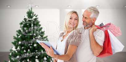 Composite image of happy couple with shopping bags and tablet pc