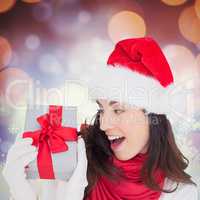 Composite image of astonished brunette in santa hat showing gift