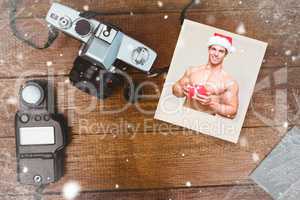 Composite image of shirtless macho man in santa hat holding gift