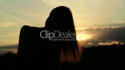 A silhouette of a woman  on a sunset comb her hair