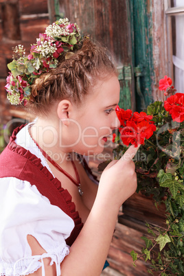 Portrait einer jungen Frau im Dirndl riechend an einer Geranie
