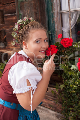 Bayrisches Mädchen im Dirndl riecht an einer Geranie .