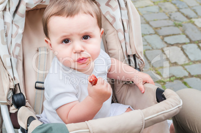 Kind im Kinderwagen ißt eine Wurst