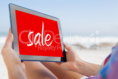 Composite image of woman sitting on beach in deck chair using ta