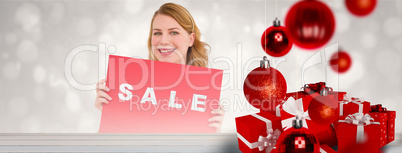 Composite image of cute blonde showing a red sale poster