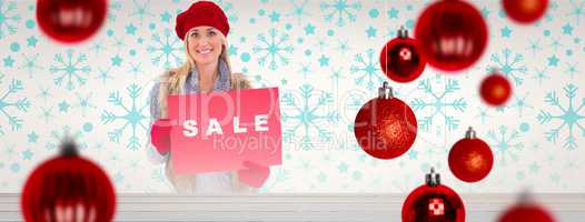 Composite image of blonde in winter clothes holding sale sign