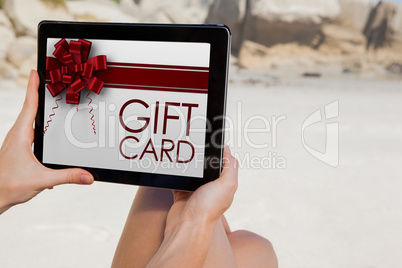 Composite image of woman sitting on beach using tablet pc