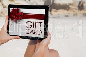 Composite image of woman sitting on beach using tablet pc