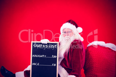 Composite image of santa sits leaned on his bag with a board