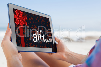 Composite image of woman sitting on beach in deck chair using ta