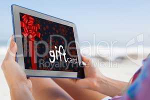 Composite image of woman sitting on beach in deck chair using ta