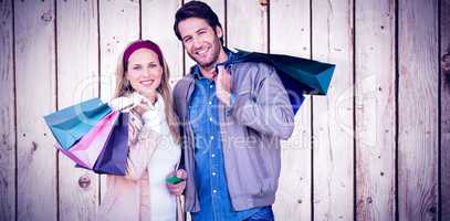 Composite image of smiling couple with shopping bags in front of