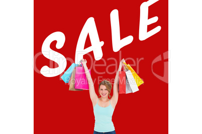 Composite image of excited blonde holding up shopping bags