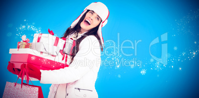 Composite image of brunette in winter clothes holding many gifts