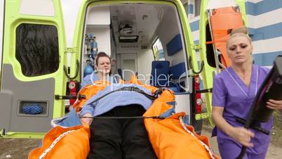 Emergency medical ambulance service paramedics crew fixing senior patient on stretcher