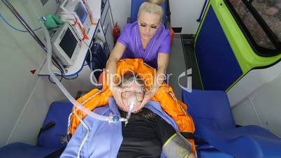 Paramedic holding patient head wearing oxygen mask in ambulance