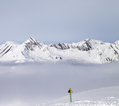 Mountains in mist and warning sing on ski slope