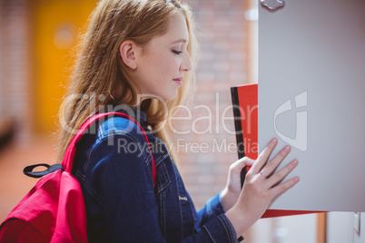Pretty student with backpack putting notebook in the locker