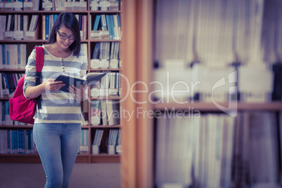 Pretty student with backpack reading a book in library