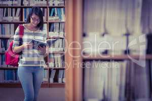 Pretty student with backpack reading a book in library