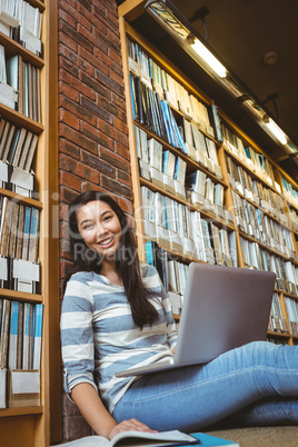 Smiling student sitting on the floor against wall in library stu