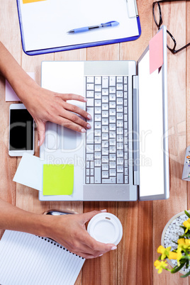 Overhead of feminine hands using laptop and holding coffee mug