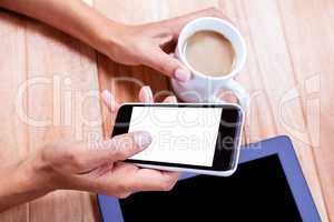 Businesswoman holding smartphone and coffee cup