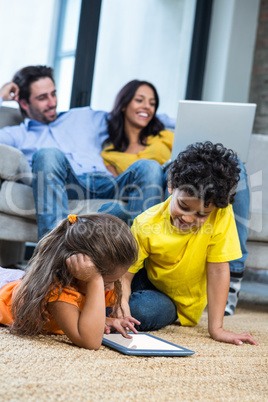 Children laying on the carpet using tablet in living room