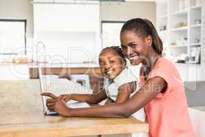 Cute daughter using laptop at desk with mother