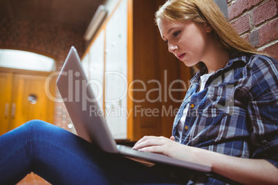 Focused student sitting on the floor against the wall using lapt