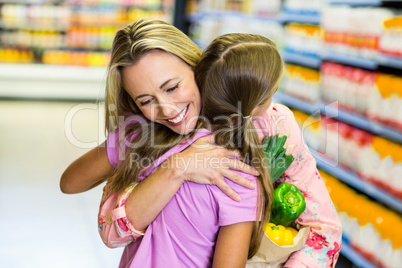 Smiling mother and daughter with grocery bag hugging