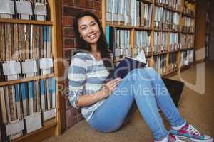 Smiling student sitting on the floor against wall in library rea
